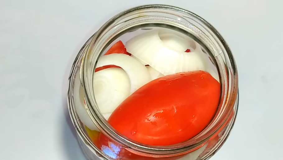 Выложите в банки половинки томатов вперемешку с луком