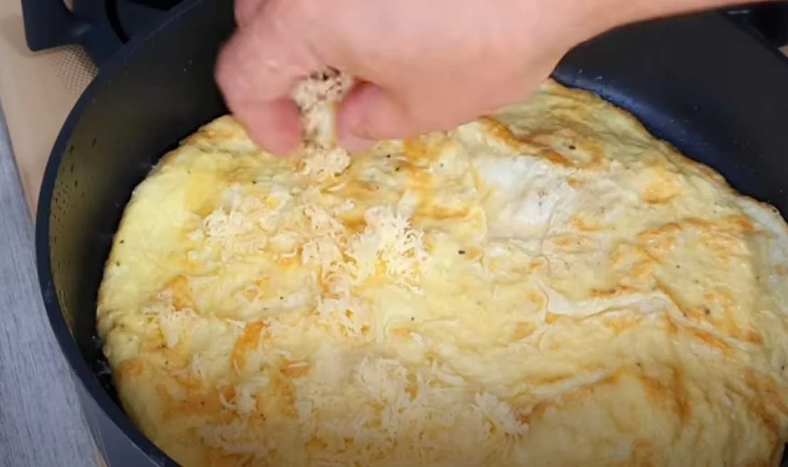 Выложите лаваш, переверните, посыпайте жареную сторону яичницы тертым сыром.