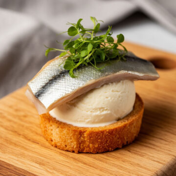 Фото: необычный гастрономический дуэт — кусочек солёной сельди на шарике ванильного мороженого, сервировка на деревянной доске