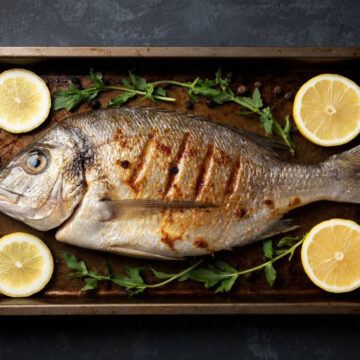 Запеченная целиком рыба с золотистой корочкой и лимоном на противне