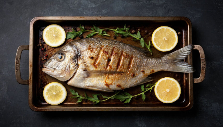 Запеченная целиком рыба с золотистой корочкой и лимоном на противне