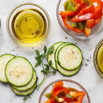 Процесс маринования свежих овощей в стеклянных мисках с травами и специями.